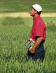 Farmer standing in a field, holding a book.